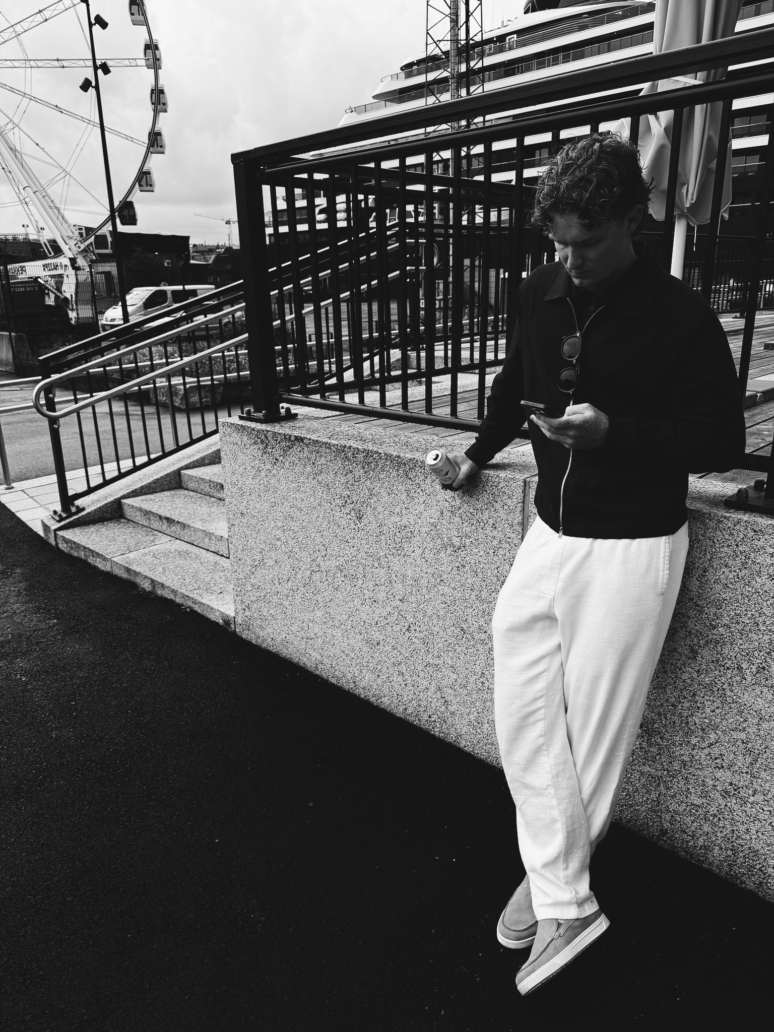 Colin in a black polo and white trousers, leaning against a wall in the city